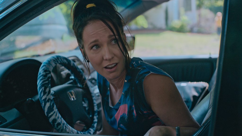 A woman with a ponytail sits in the driver's seat of a Honda car, looking to her left with a surprised expression.