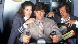 Three people in a cockpit, one man holding controls with a serious expression, a woman and another man look on with concern in an airplane setting.