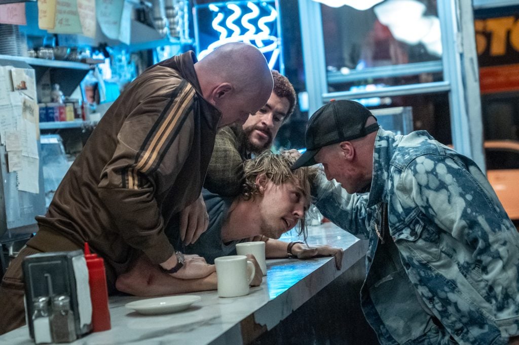 Four men confront each other aggressively at a diner counter, with one man held down by two others while a fourth leans in close, all with tense expressions.