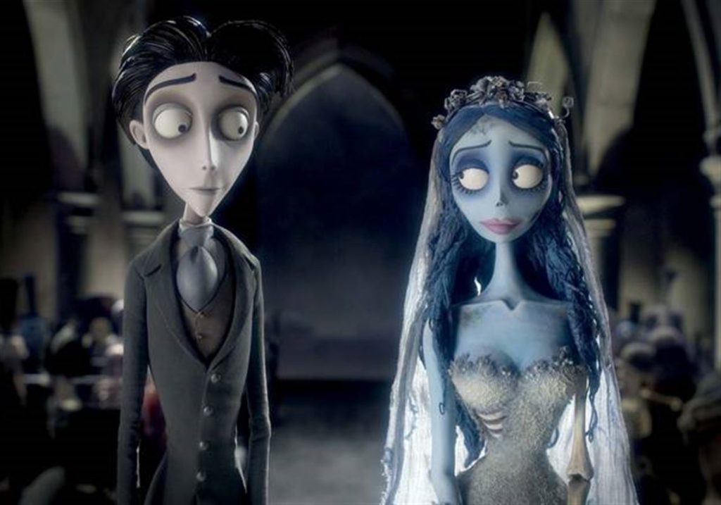 Two animated characters, a pale man in a suit and a blue-skinned woman in a wedding dress, stand side by side in a dimly lit, gothic setting.
