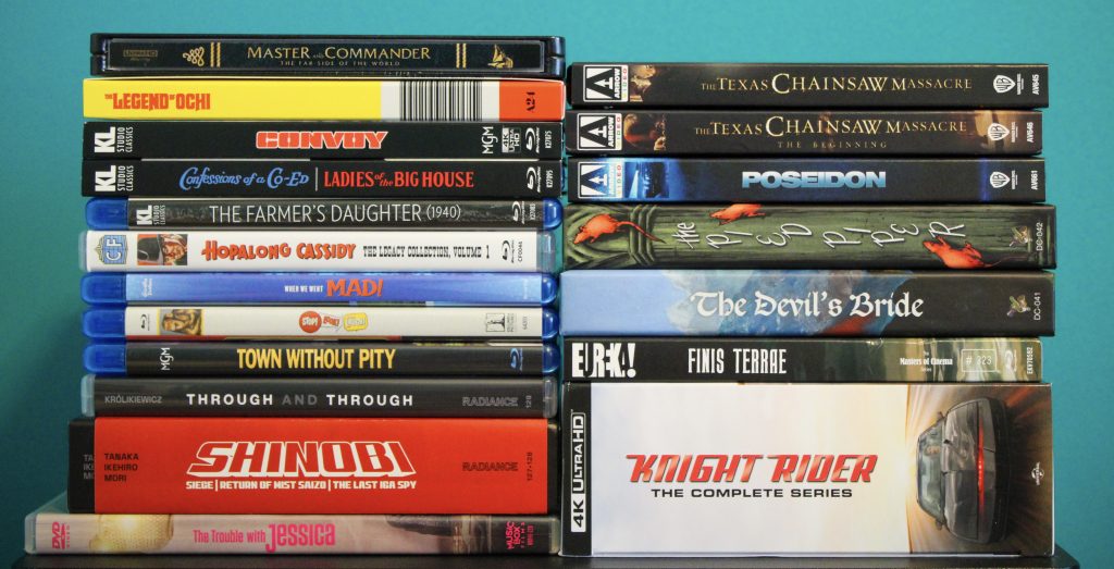 A stack of DVDs and Blu-rays featuring various movie and TV titles, including "Master and Commander," "The Texas Chainsaw Massacre," "Knight Rider," and "Shinobi.