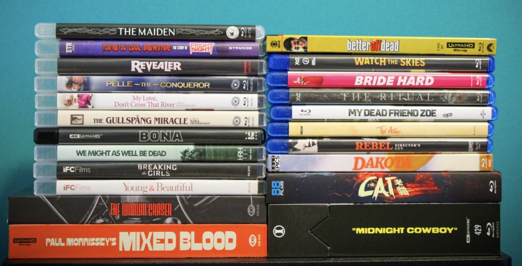 A collection of DVD and Blu-ray movie cases arranged in two stacks against a blue background, featuring various film titles and genres.