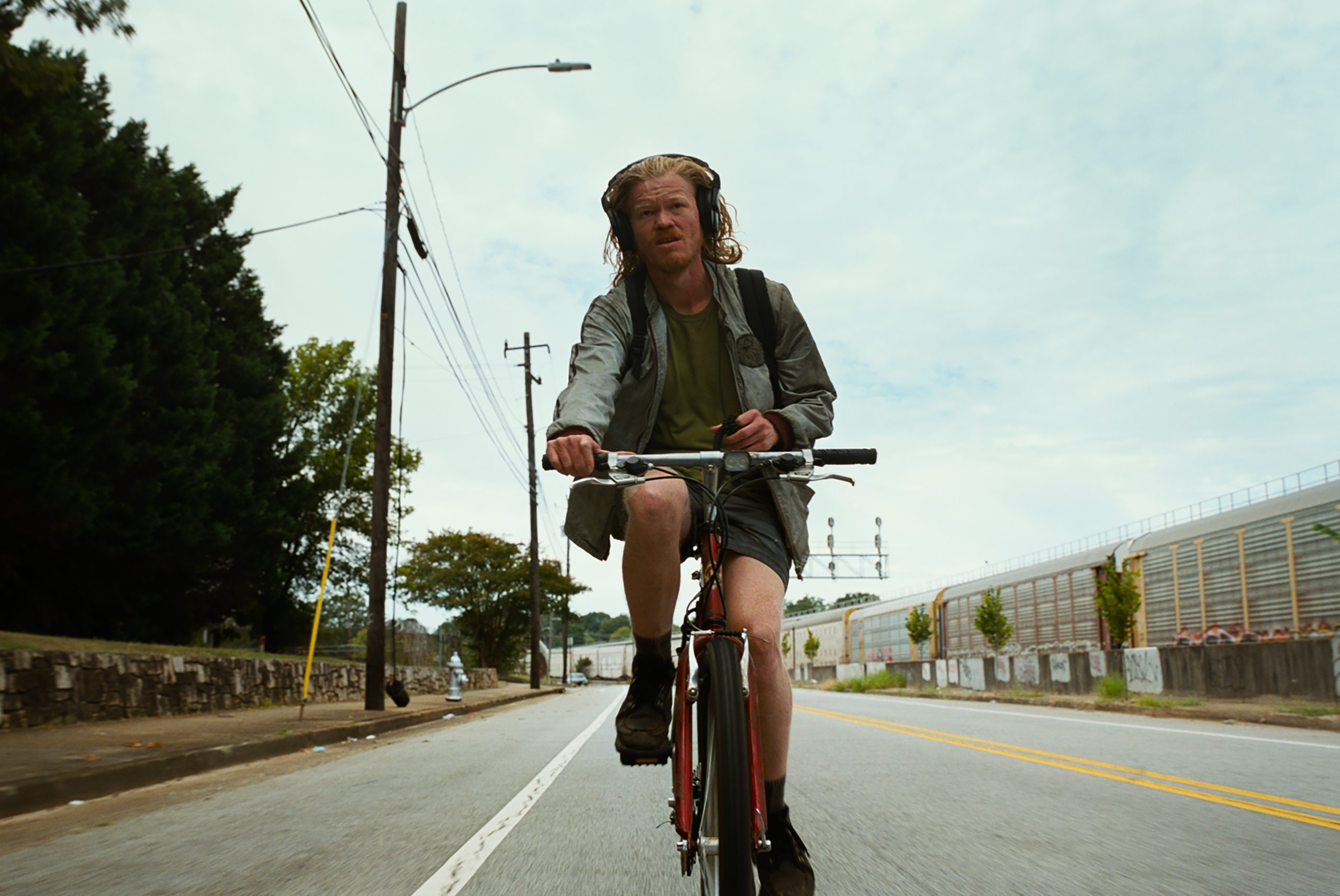A person wearing headphones and a backpack rides a bicycle down an empty street on a cloudy day.