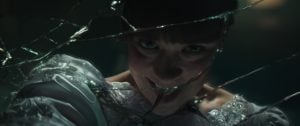 A person in a white dress leans close to a broken mirror, their reflection fragmented by the shards, with a dramatic and intense expression.