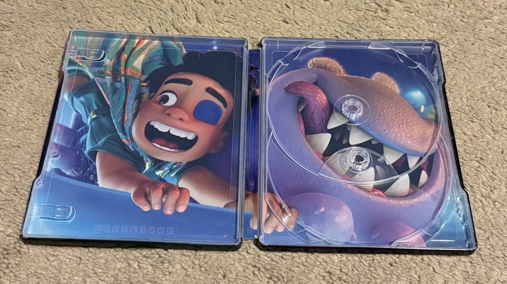 An open Blu-ray case displays animated characters: a boy with a patch on his eye on the left, and a smiling sea monster's face on the right. No disc is present.