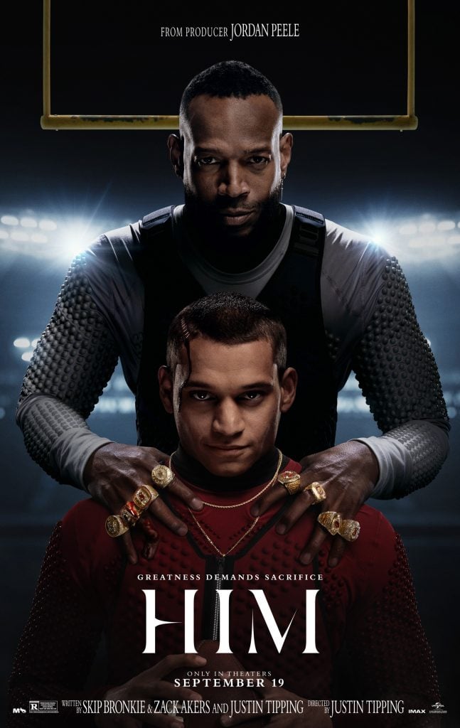 Two men pose in a dramatic, stadium-lit setting; one stands behind the other with hands on his shoulders. The poster text reads "HIM" and "Greatness Demands Sacrifice.