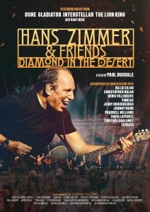 Hans Zimmer playing guitar on stage with his band, with text promoting the concert film “Hans Zimmer & Friends: Diamond in the Desert.”.