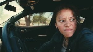 2026 Oscar Winner Predictions A person with a tense expression sits in the driver's seat of a car, looking out the open door.