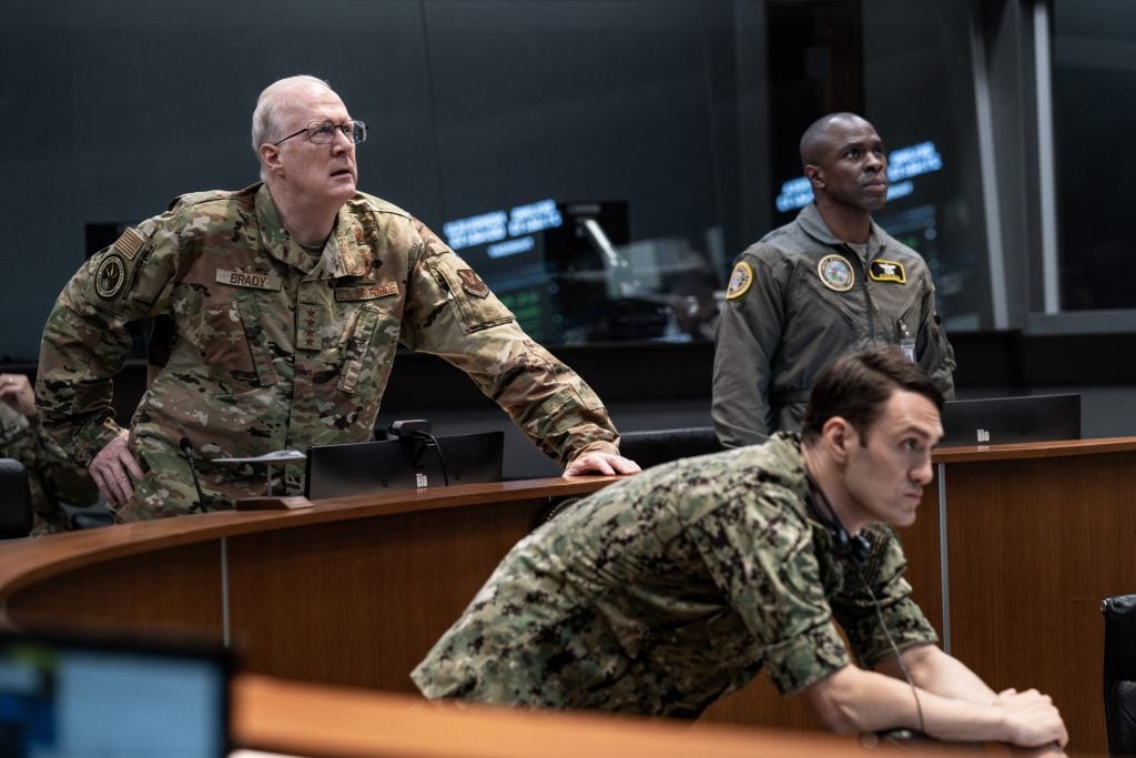 Three military personnel in uniform monitor computer screens in a command center, appearing focused and attentive to ongoing operations.