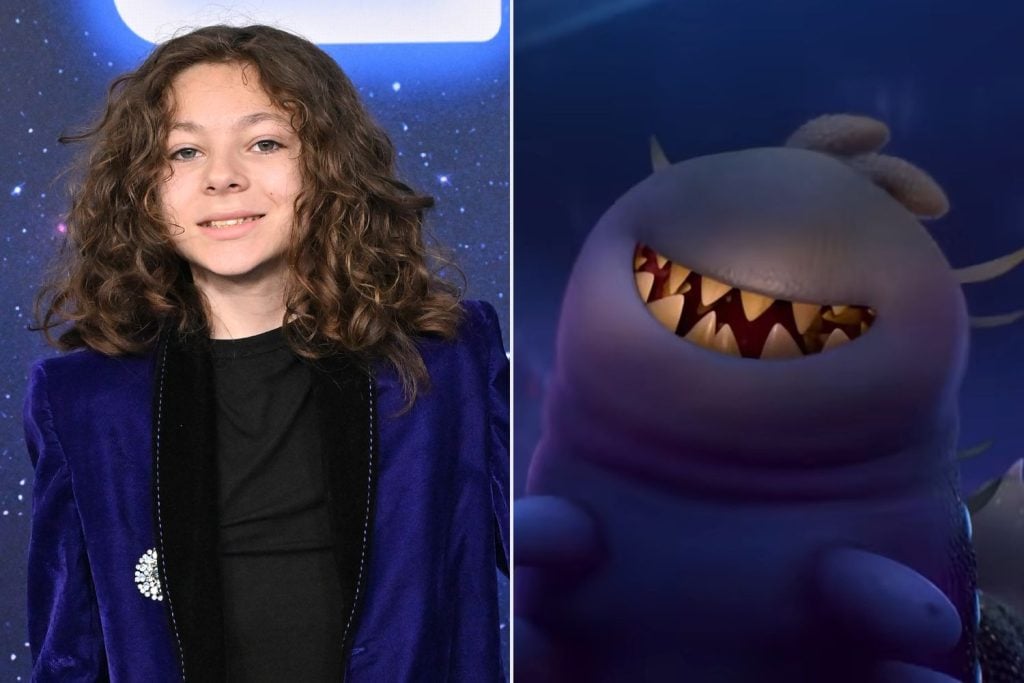 A person with long curly hair in a blue jacket stands next to an animated shark-like character with sharp teeth.