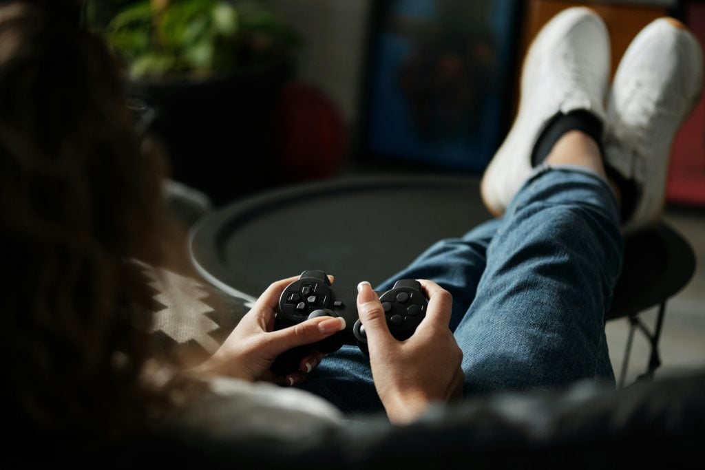 A person sitting with legs crossed on a table, holding a game controller and playing a video game.