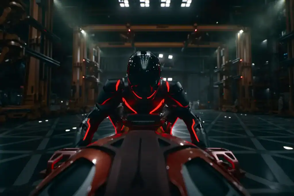 A person in a black and red futuristic suit leans over a high-tech vehicle in a large, industrial, dimly lit facility.
