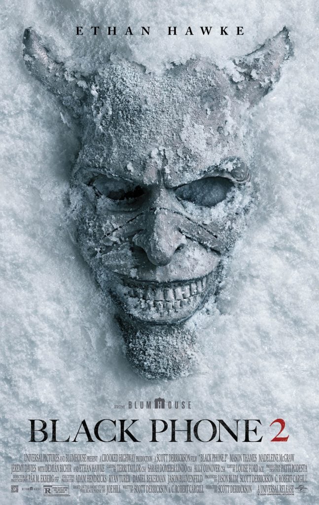 A snow-covered demonic mask with sharp features lies partially buried, with the text "Black Phone 2" and actor Ethan Hawke’s name above.