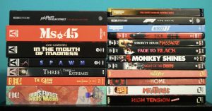No Streaming Required: Physical Media Spotlight For The Week Of October 14th A stack of various Blu-ray and DVD movie cases arranged in two columns against a turquoise background.
