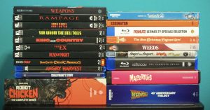 A collection of DVD and Blu-ray cases stacked side by side, featuring movies, TV shows, and boxed sets against a teal background.