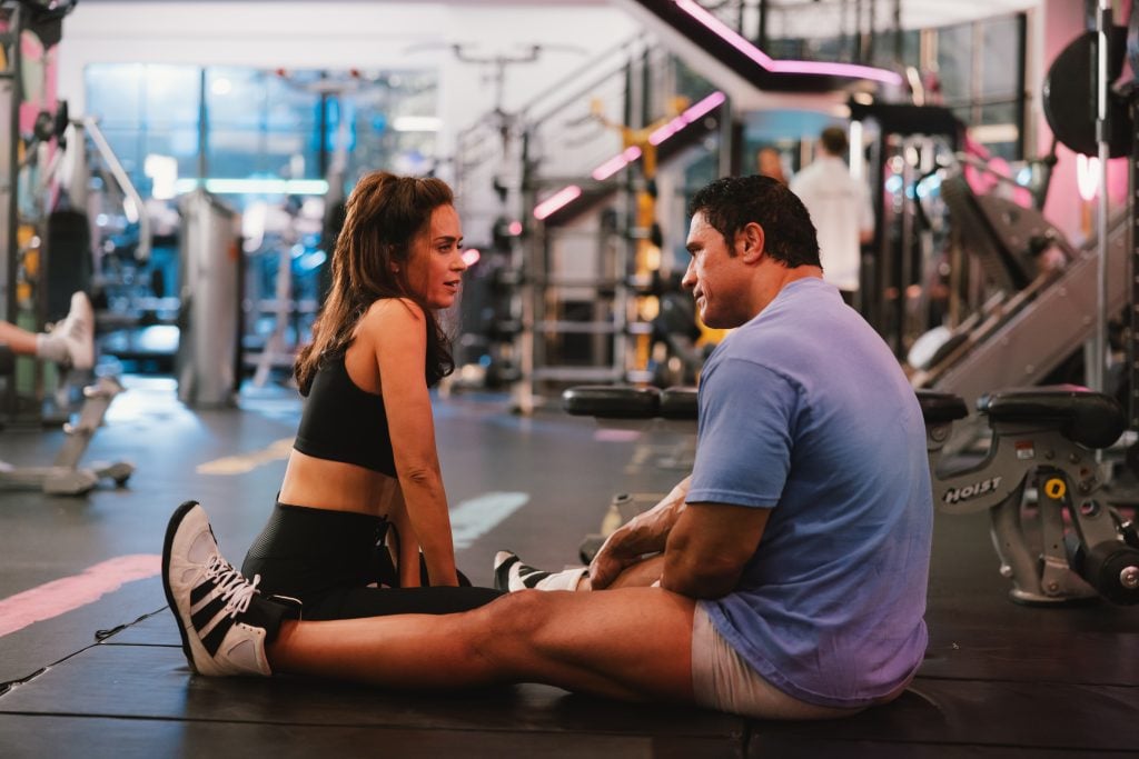 A man and woman sitting on a gym floor.