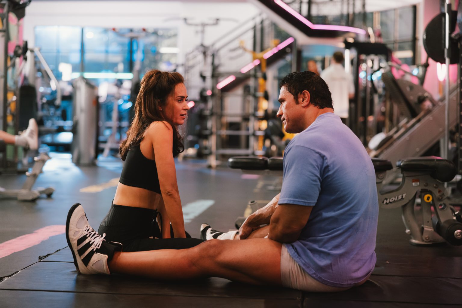 A man and woman sitting on a gym floor.