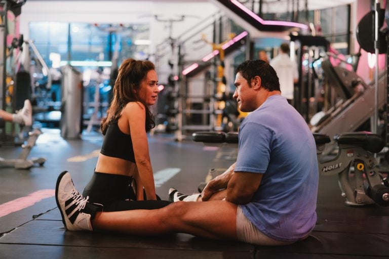 A man and woman sitting on a gym floor.