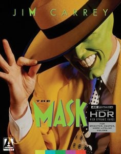 A person in a yellow suit and hat with a bright green face smiles widely while tipping the hat. The text reads "The Mask" and highlights 4K Ultra HD features.