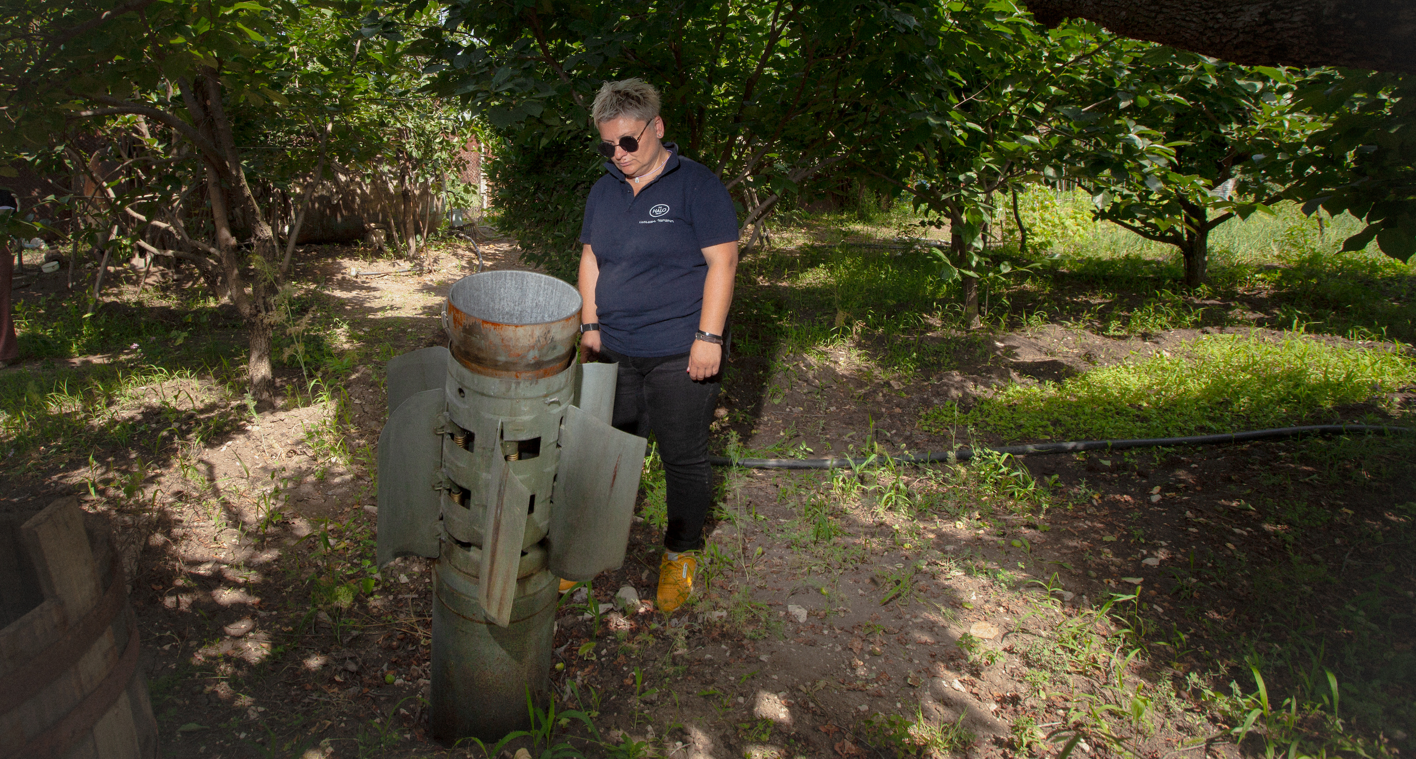A person stands in a shaded, grassy yard, looking down at an unexploded missile embedded in the ground.