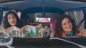 Universal To Release Family Film ‘Gabby’s Dollhouse: The Movie’ On Blu-Ray This November Two women sit in the front seats of a car, one reading a map with cat illustrations. A stuffed cat toy is visible between them on the dashboard.