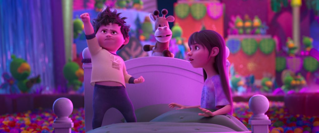 Two animated children sit on a bed in a colorful, candy-themed room; one raises a fist confidently while the other looks surprised. A toy animal sits between them.
