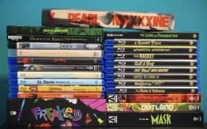 A collection of Blu-ray and DVD movie and TV show cases, stacked vertically and horizontally in two piles against a teal background.