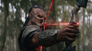 An alien creature aims a high-tech bow with red laser sights in a forest setting, wearing armor and focusing intently on a target.