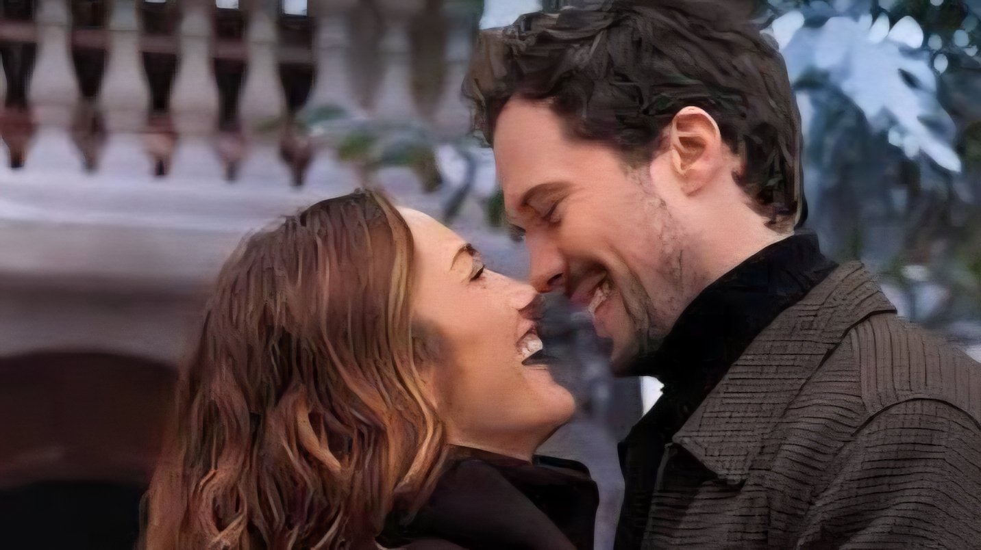 A man and woman stand close together outside, smiling and touching noses with joyful expressions.