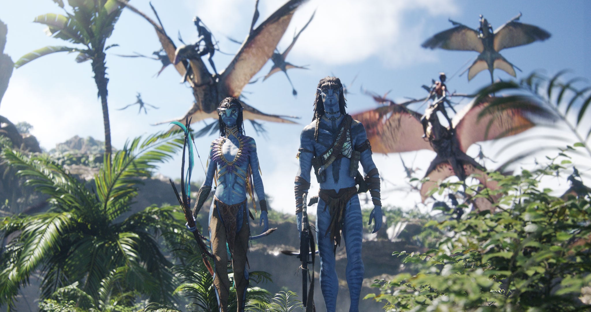 Two blue-skinned humanoid figures walk through dense jungle while flying creatures and riders soar in the sky behind them.