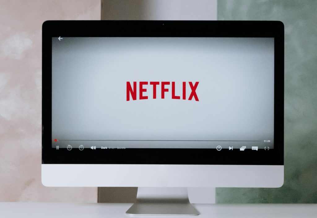 A computer monitor displays the Netflix logo on its screen, with a video playback bar visible at the bottom.