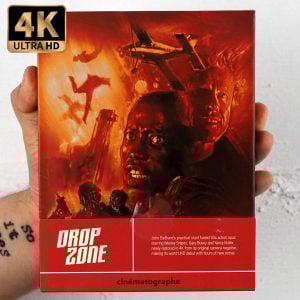 A hand holds a 4K Ultra HD edition of the movie "Drop Zone," featuring an action-packed cover with three intense faces, a parachute, and explosions in the background.