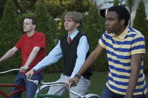 Lionsgate To Release The Cult Comedy Favorite ‘Mystery Team’ On Blu-Ray This January Through The Vestron Line Three young men stand outdoors holding bicycles, looking ahead with serious expressions. Green trees and part of a white house are visible in the background.