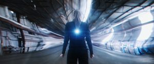 A person with long hair stands in a futuristic, distorted tunnel with a glowing light on their back.