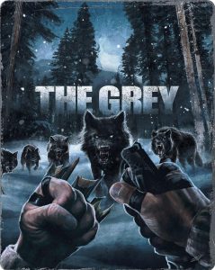 A person faces a pack of aggressive wolves in a snowy forest, holding sharp objects in their fists. The text "THE GREY" appears at the top.
