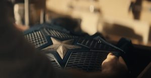 A close-up of a person holding a dark blue armored vest featuring a silver star emblem and textured plating.