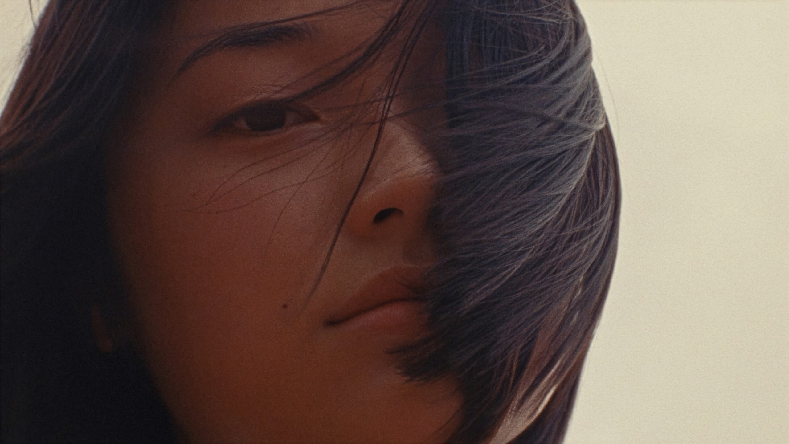 Close-up of a person's face with long hair partially covering one eye, looking directly at the camera with a neutral expression.
