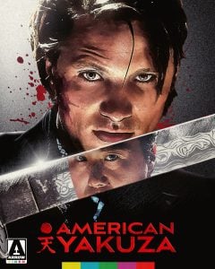 A man’s face is shown above a large knife reflecting another man’s face; blood splatters are in the background. Text reads "American Yakuza" with Japanese characters and logo at the bottom.