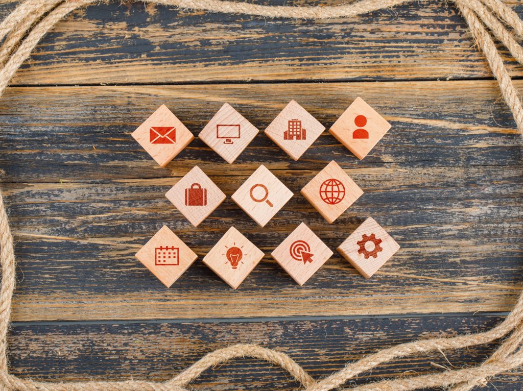 Wooden blocks with business and communication icons arranged in rows on a rustic wooden surface, framed by coiled rope.