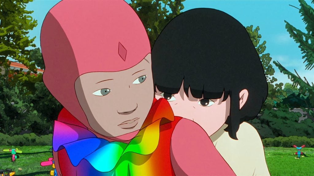 Two animated characters, one wearing a pink helmet and rainbow-colored scarf, sit close together outdoors with greenery in the background.