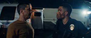 IFC, Shudder & RLJE Unveil Stacked 2026 Slate – Star-Studded Thrillers, Cults & Cursed Artifacts Incoming Two men stand facing each other at night; one is a police officer with a bruised face, wearing a uniform, while the other wears a brown shirt.