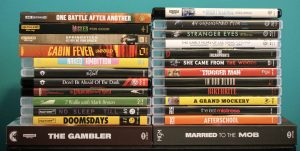 Two stacks of DVD and Blu-ray movie cases are arranged side by side against a teal background, showing various film titles on their spines.