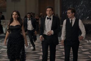 Four people in formal attire walk with purpose across a checkered marble floor in an elegant, dimly-lit room.