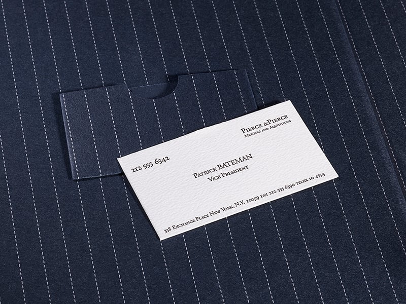 A business card reading "Patrick Bateman, Vice President, Pierce & Pierce" rests on a dark pinstripe suit.