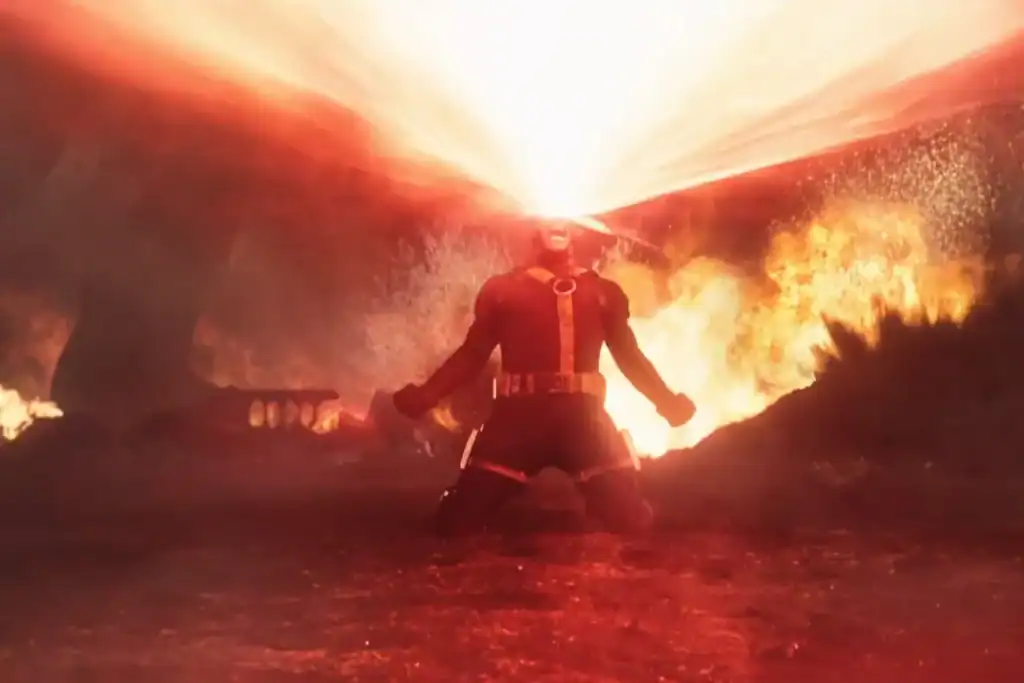 A person kneels on the ground with beams of intense red energy shooting from their eyes, surrounded by fire and a smoky, red-lit background.