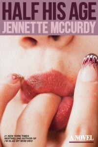 A close-up of a person's lips and fingers with detailed nail art; text above reads "HALF HIS AGE JENNETTE MCCURDY," and below promotes a novel by the bestselling author.