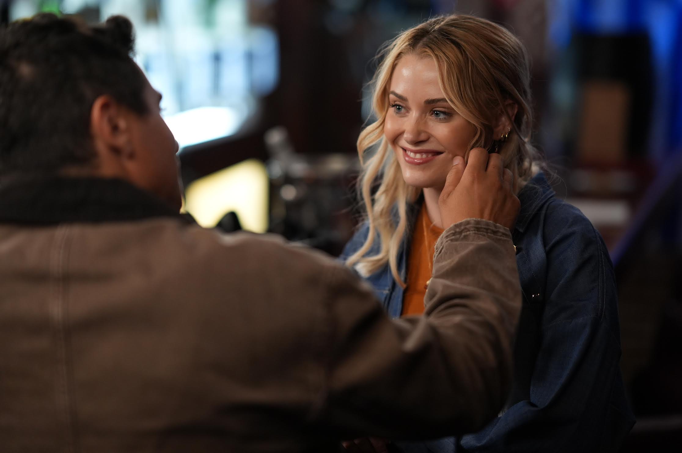 A man touches a smiling woman's face while they sit together in what appears to be a bar or cafe.