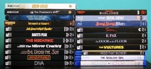 Two stacks of various movie cases, including 4K UHD, Blu-ray, and DVD formats, arranged side by side against a blue background.