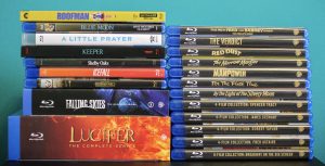 A collection of Blu-ray and DVD cases, including TV series and movie collections, stacked against a blue background.