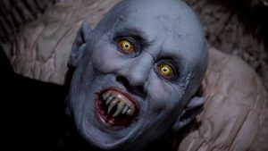 A bald, pale figure with pointed ears, yellow glowing eyes, and sharp fangs bares its teeth in a menacing expression.